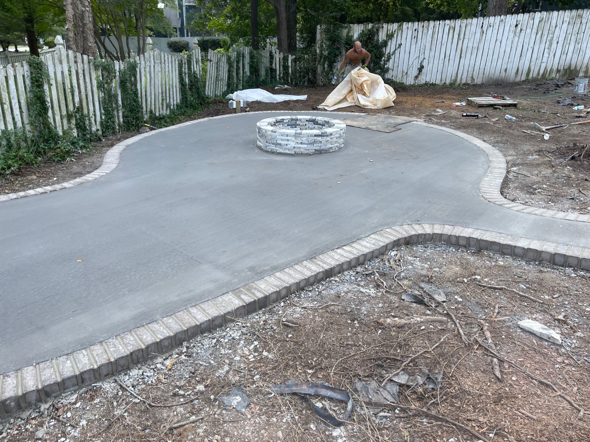 Newly poured concrete patio with a fire pit and brick border in a yard.