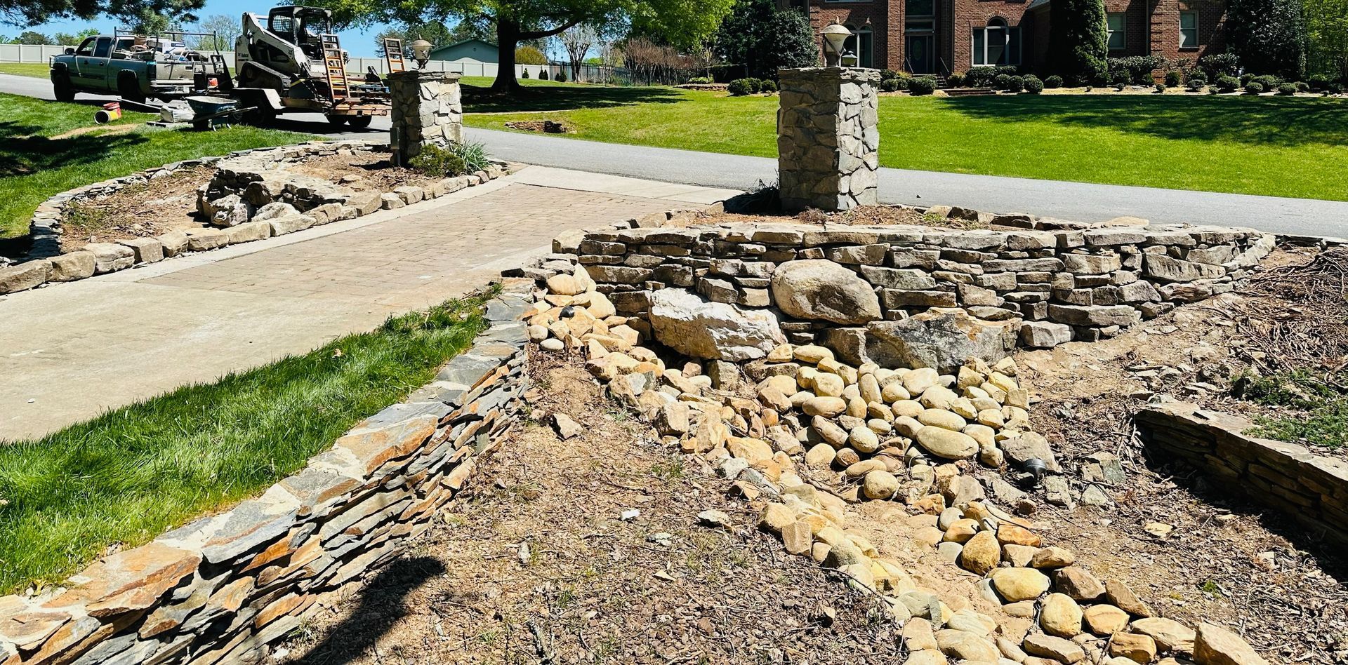 Driveway entrance with stone pillars, gravel pathway, and landscaped stone features.