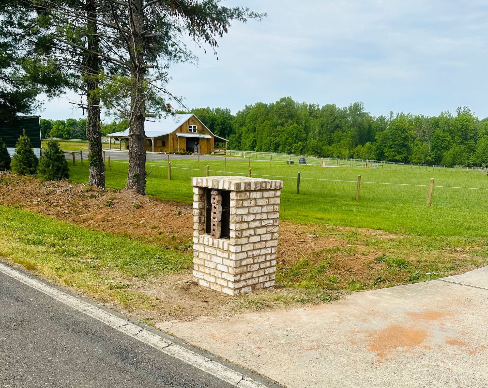 Brick mailbox on a corner, yellow barn and green field in the background.