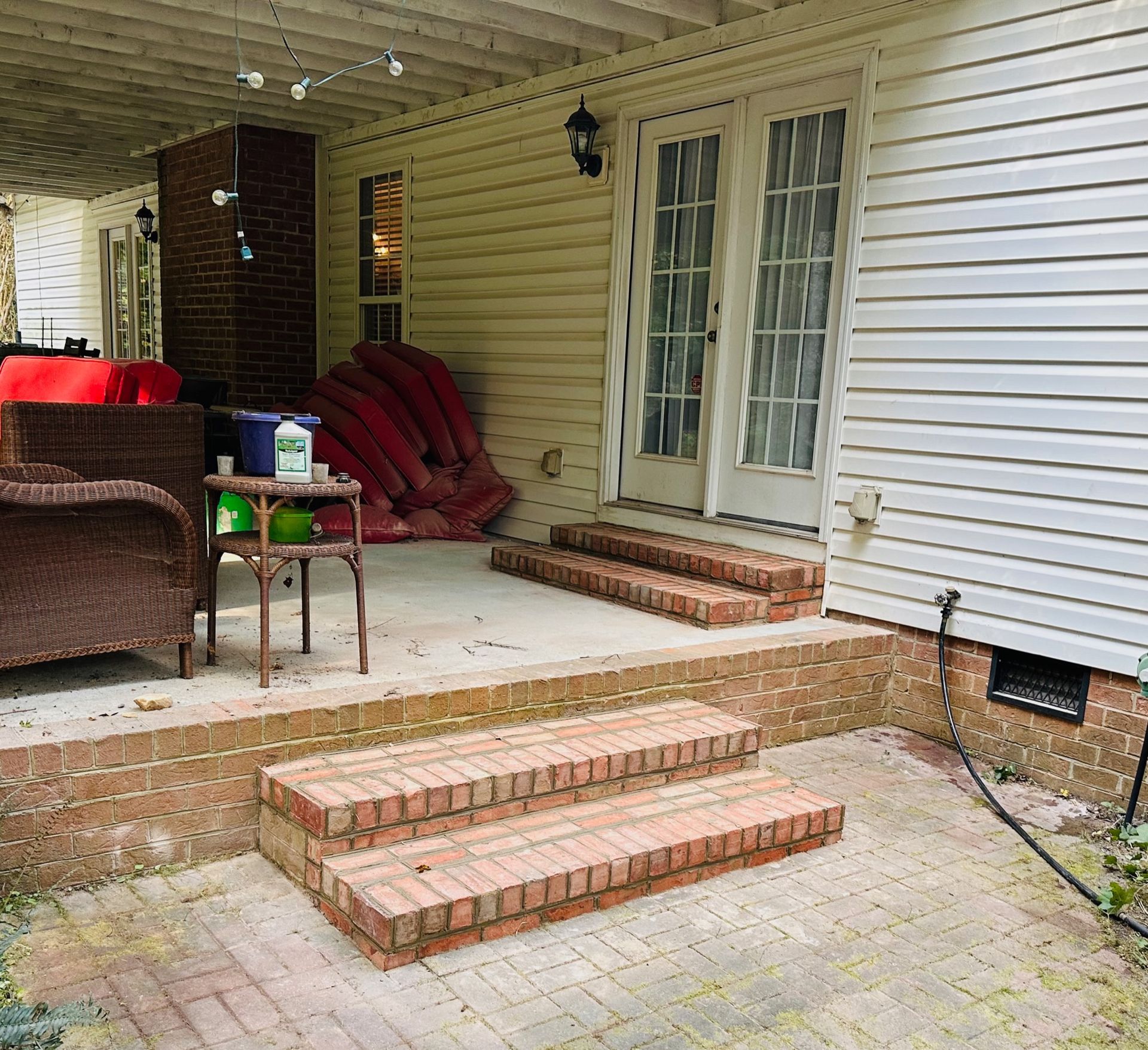 Brick patio with steps leading to French doors, flanked by a brick base and white siding.
