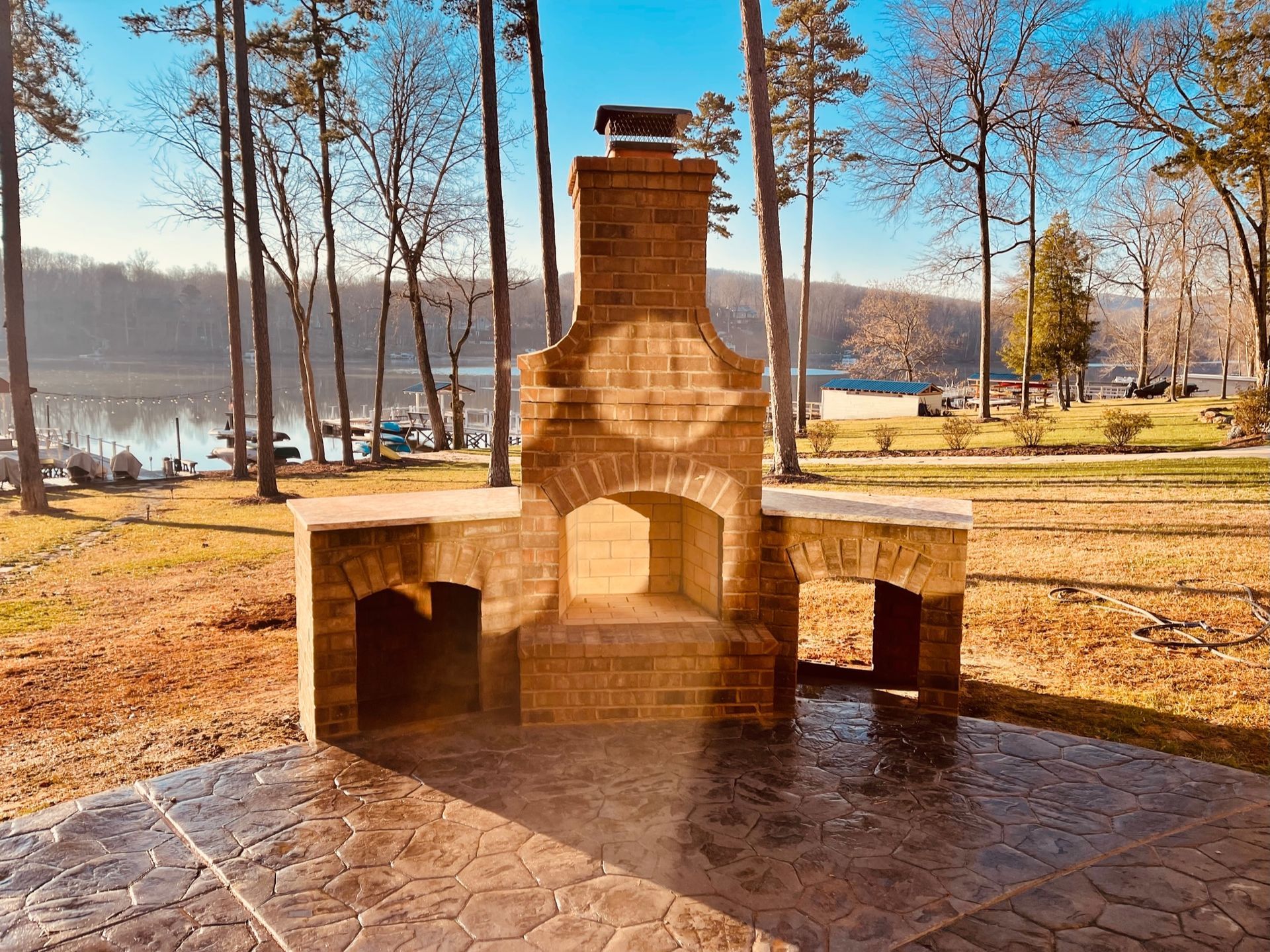 Brick outdoor fireplace with side counters on a patio overlooking a lake.