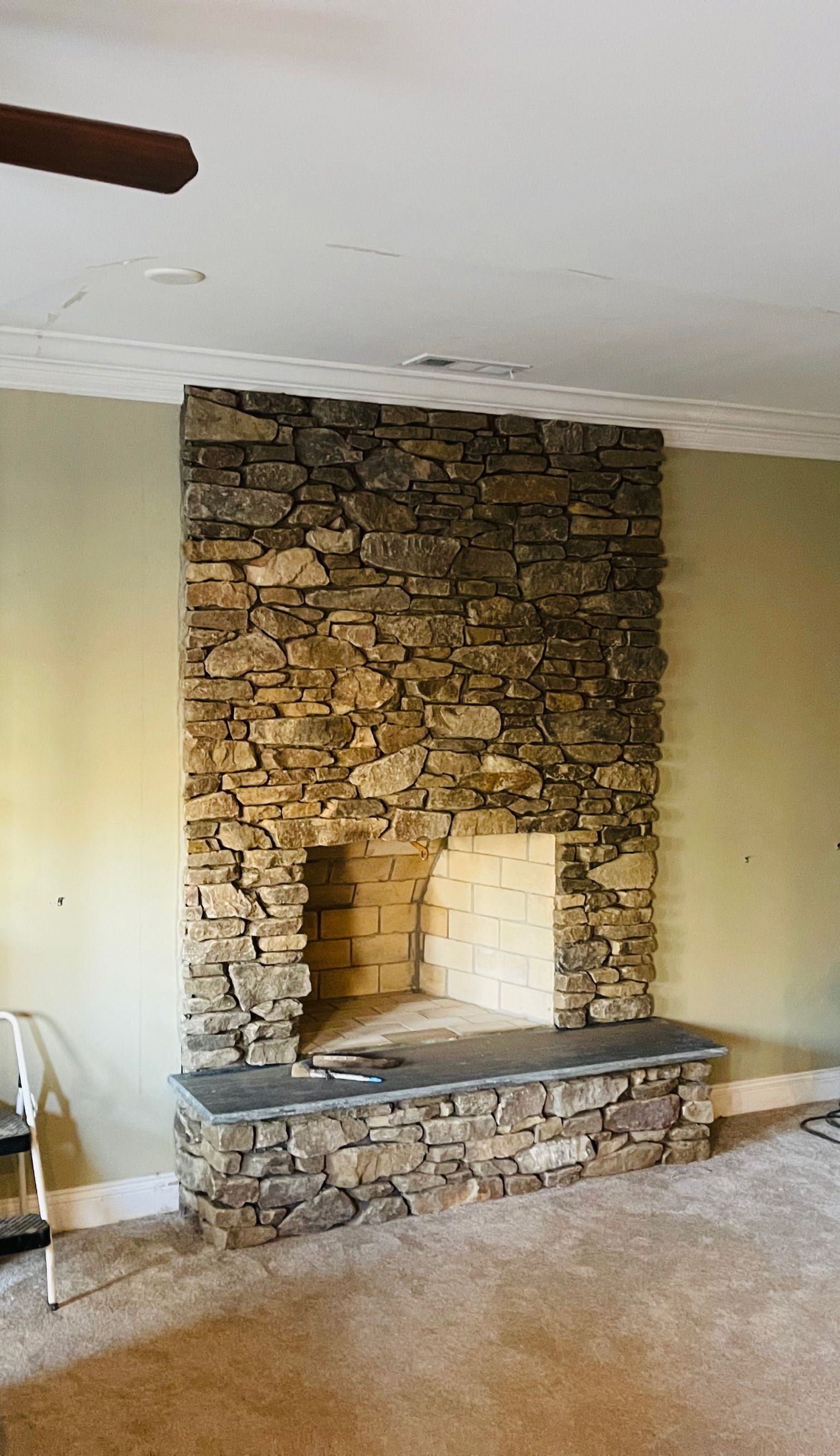Stone fireplace with hearth, surround, and opening against a light green wall in a room.