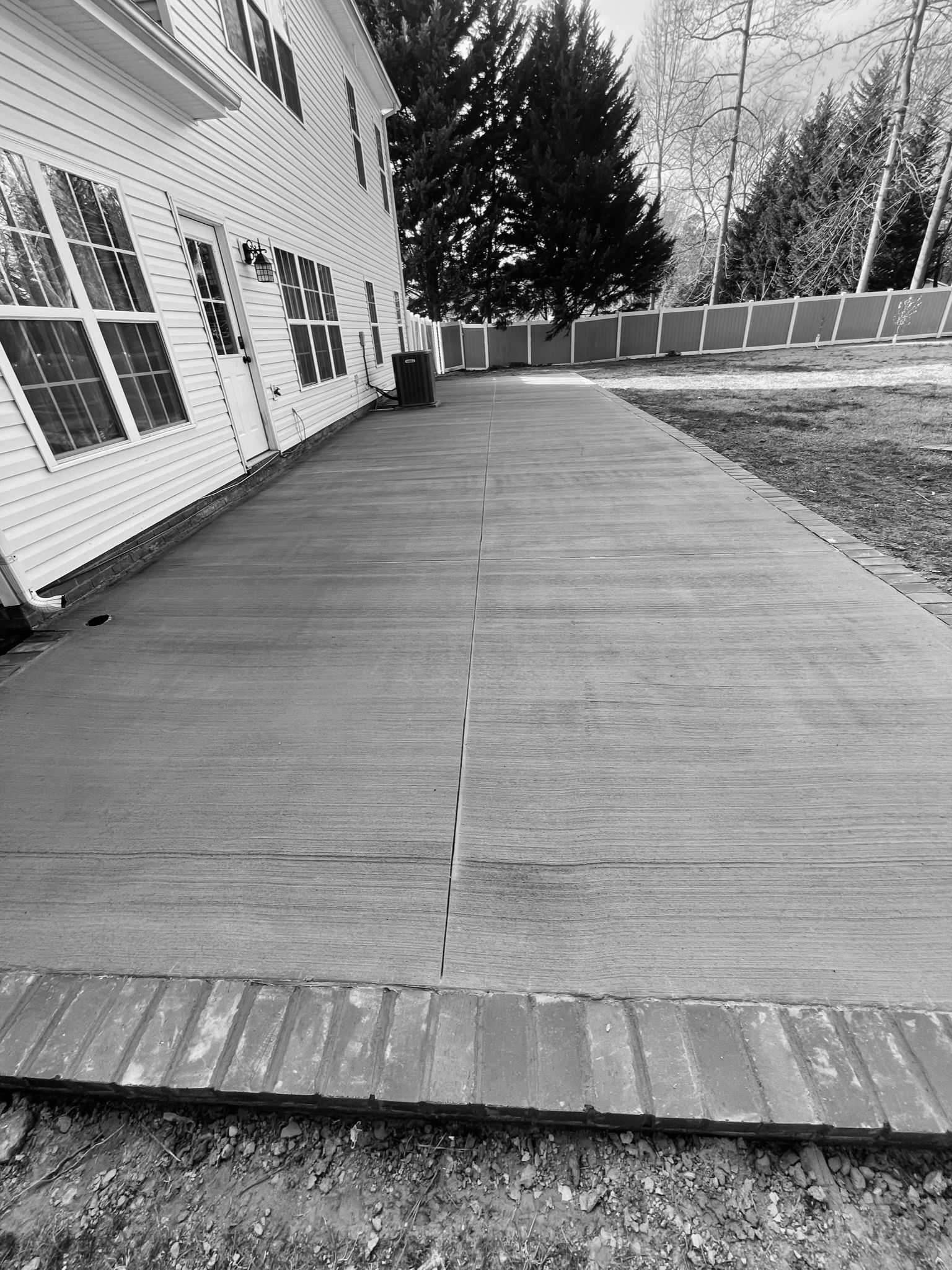 Black and white photo of a concrete patio next to a house, bordered by brick.