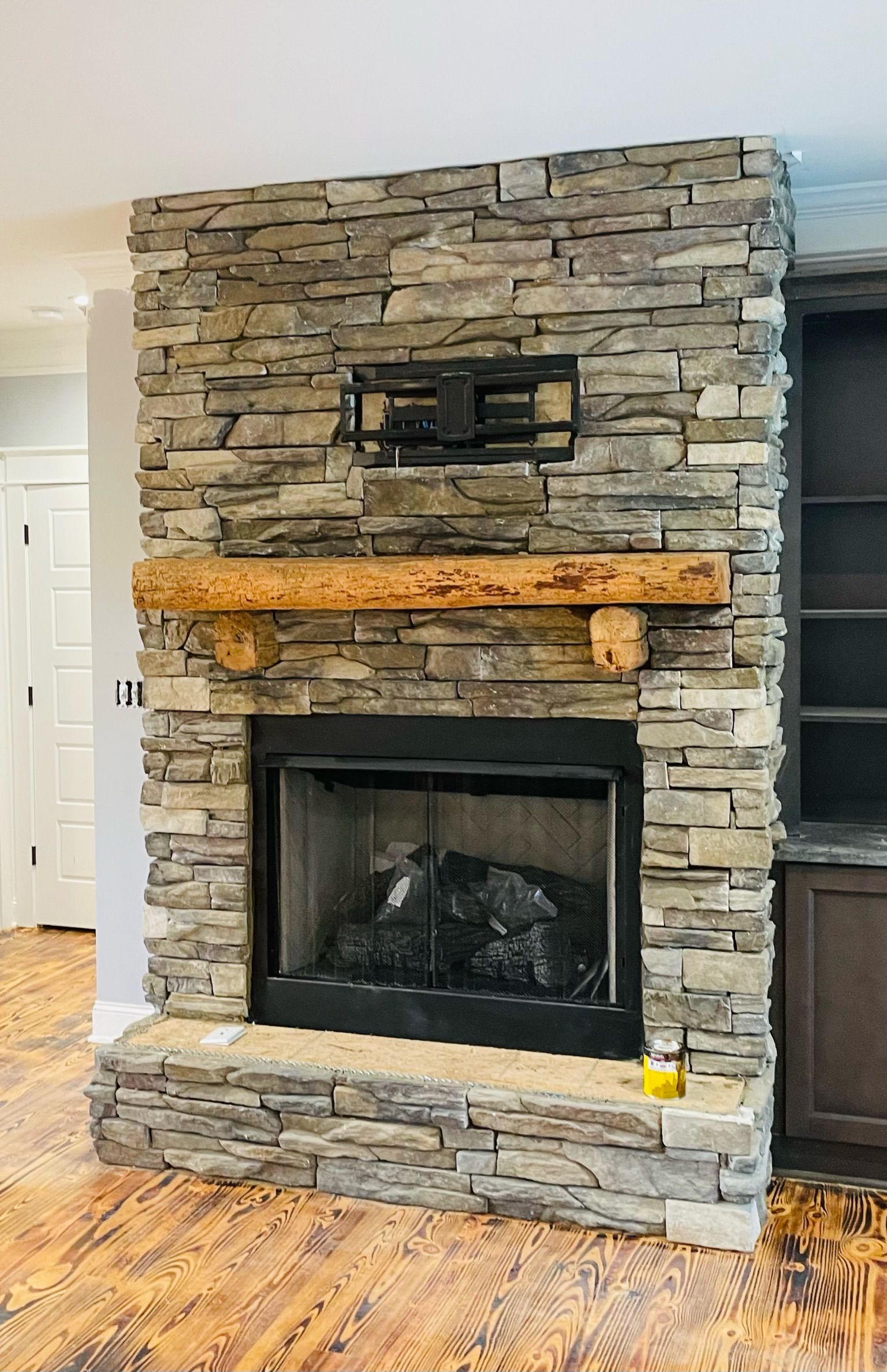 Stone fireplace with wooden mantel, black firebox, and mounted TV bracket.