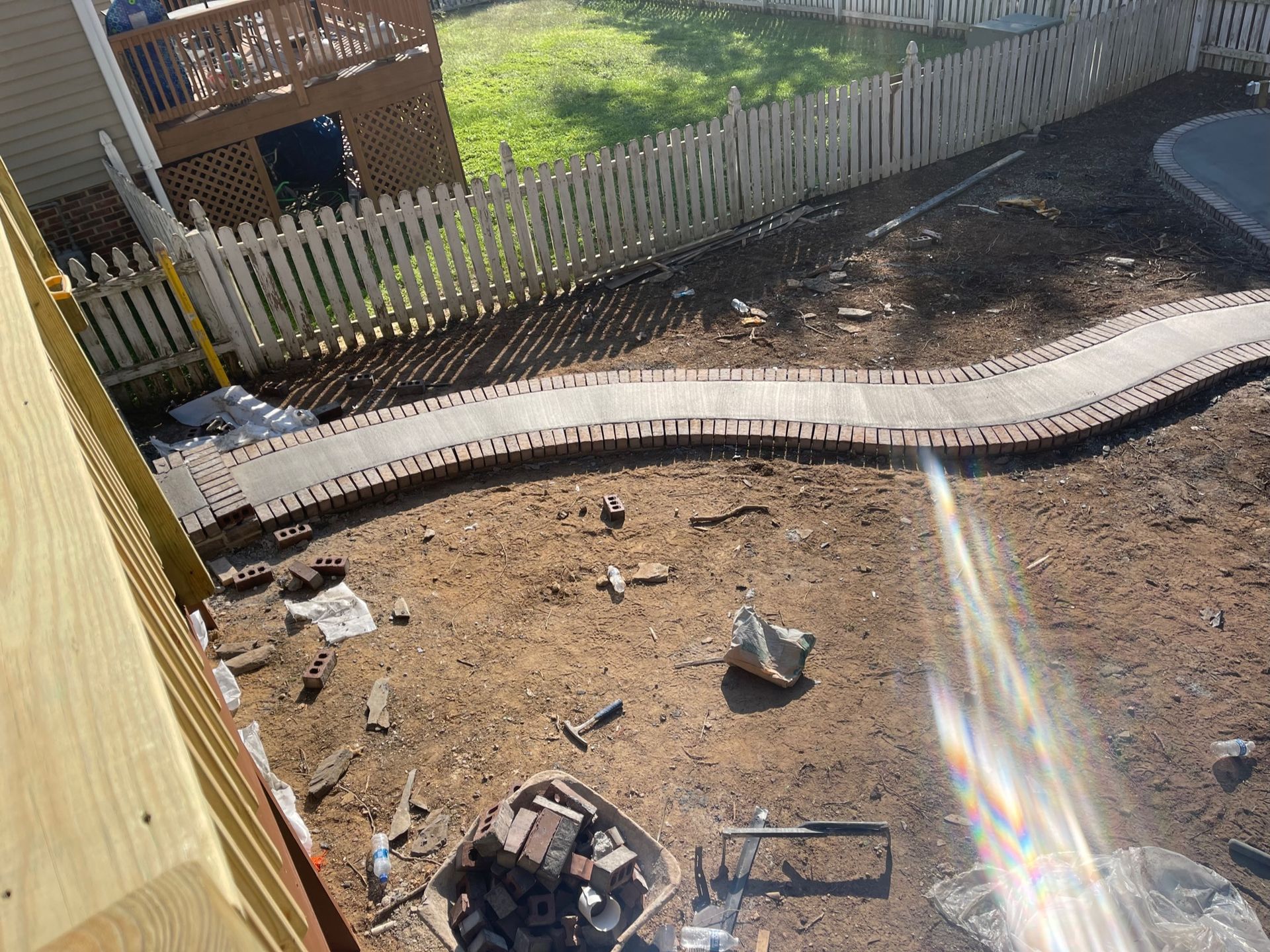 Backyard under construction with a brick path, fence, and tools.