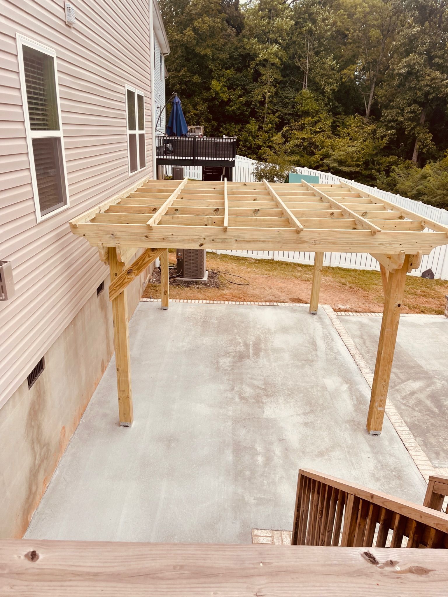 A wooden pergola attached to a house, over a concrete patio.