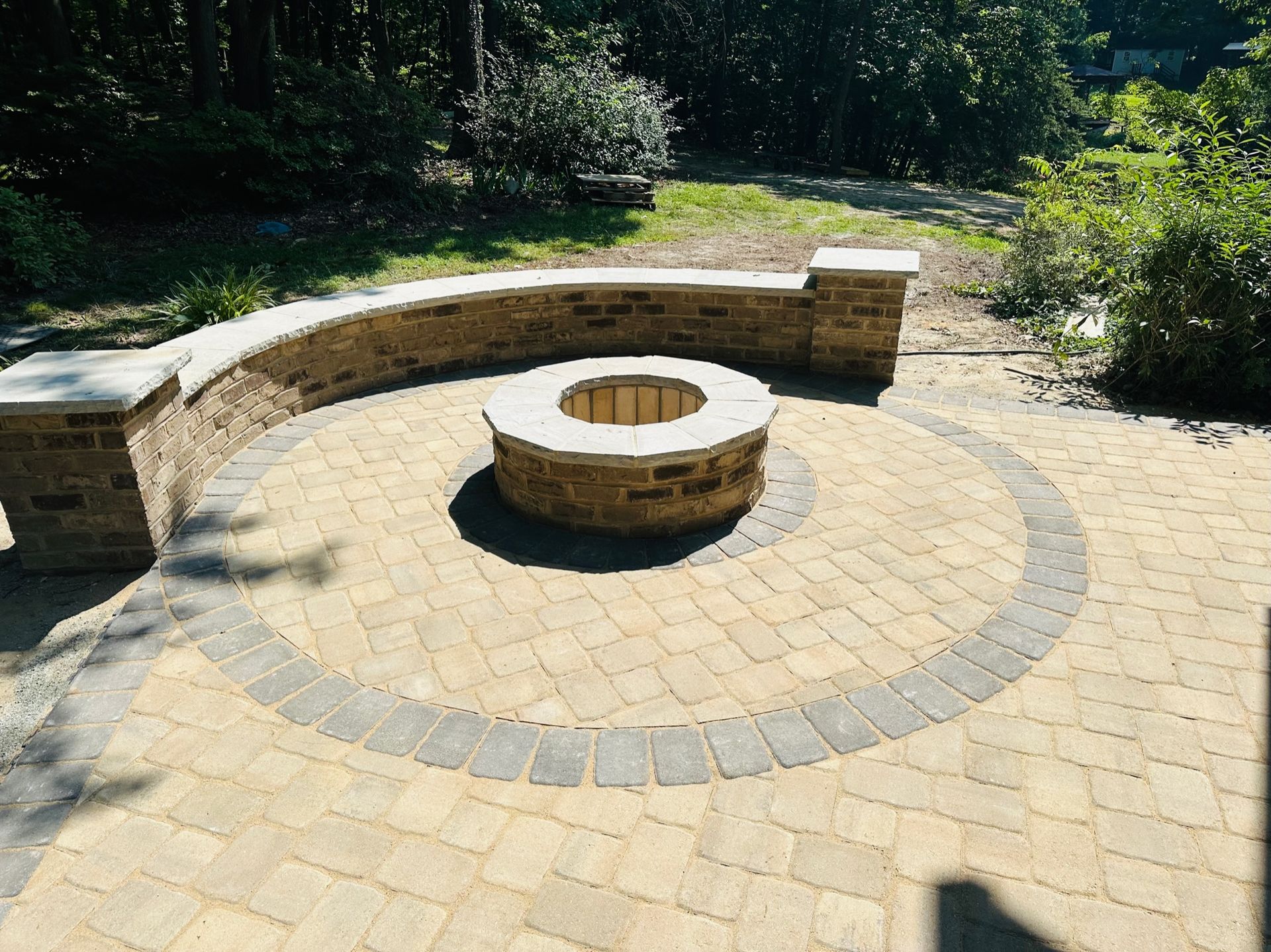 Brick fire pit with a curved brick bench on a stone patio, in an outdoor setting.