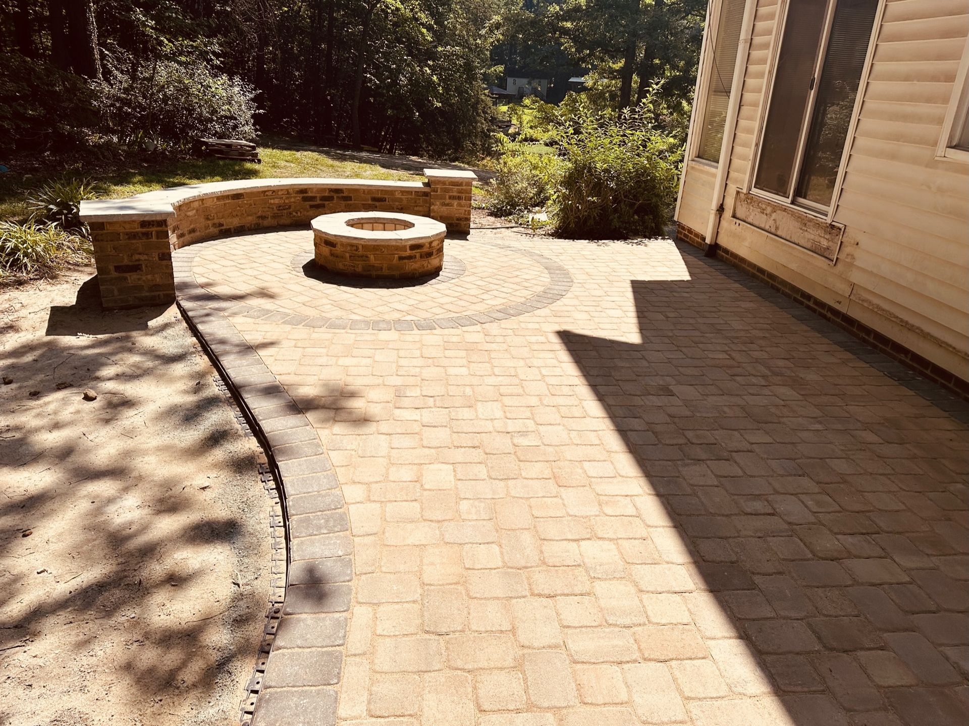 Brick patio with fire pit, seating wall, and house; tan, brown, and grey colors.