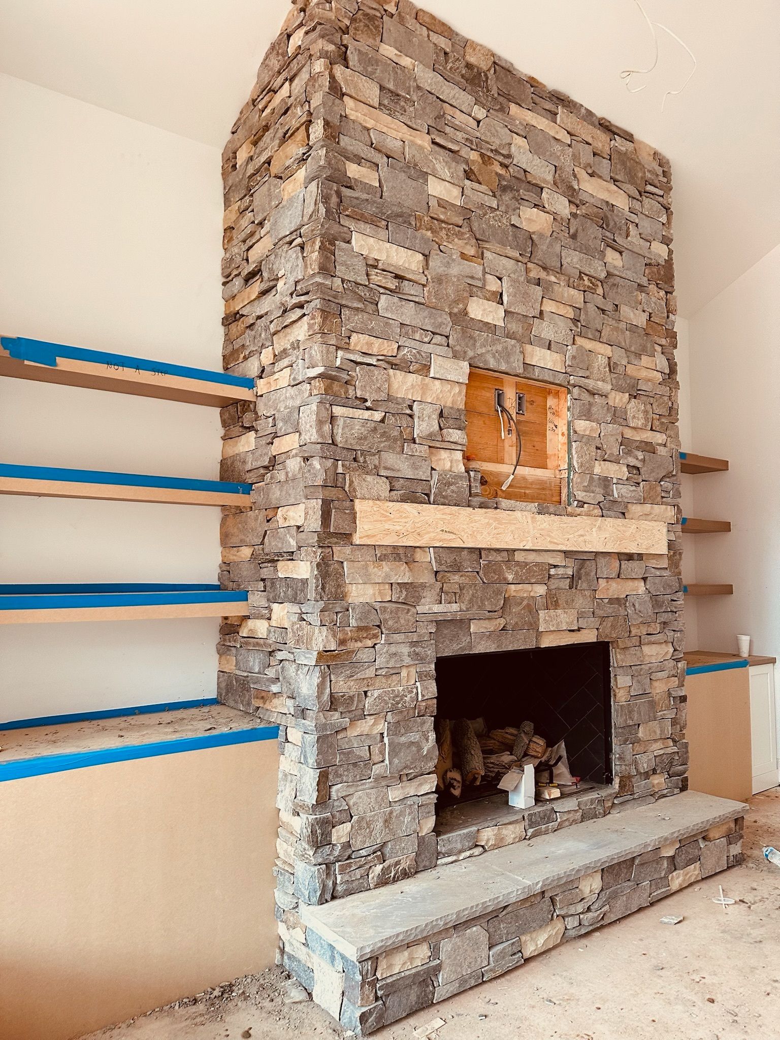 Stone fireplace with built-in shelves under construction, tan, gray, and brown tones.