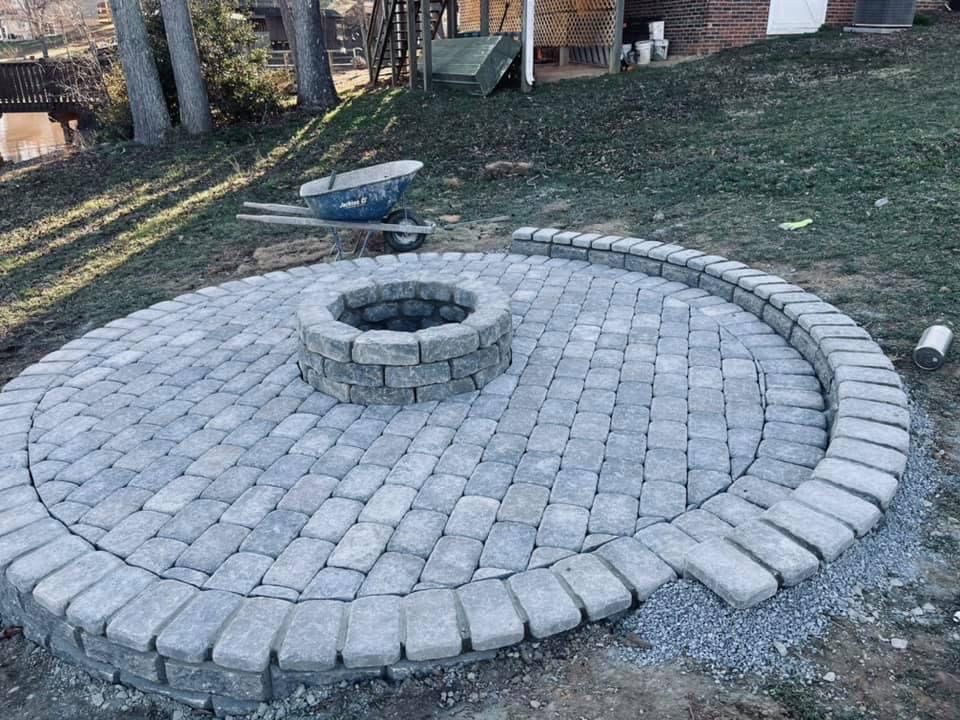 Circular stone patio with fire pit in center, surrounded by a curving border on a grassy yard.