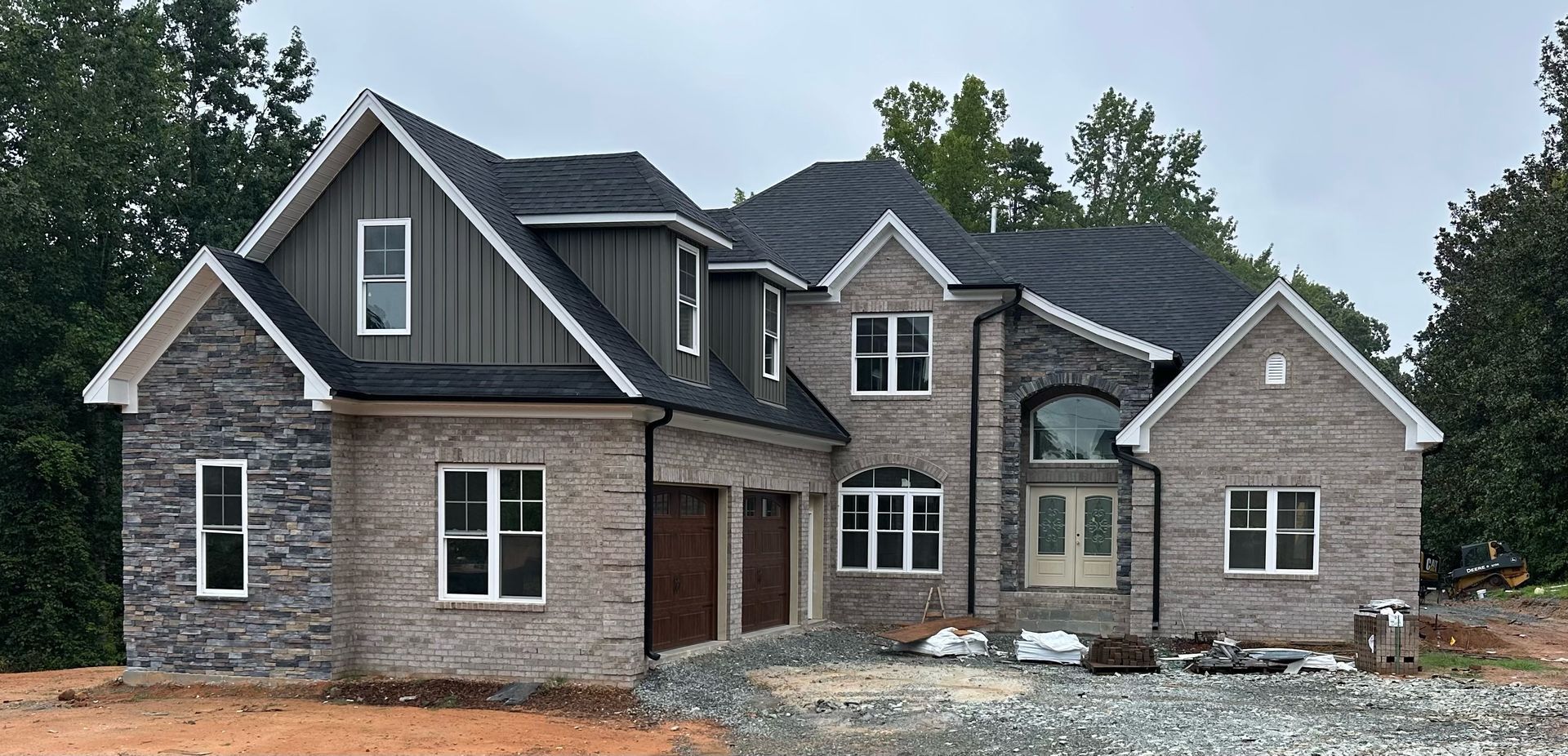 A two-story house under construction; gray brick exterior, dark roof, and two car garage.