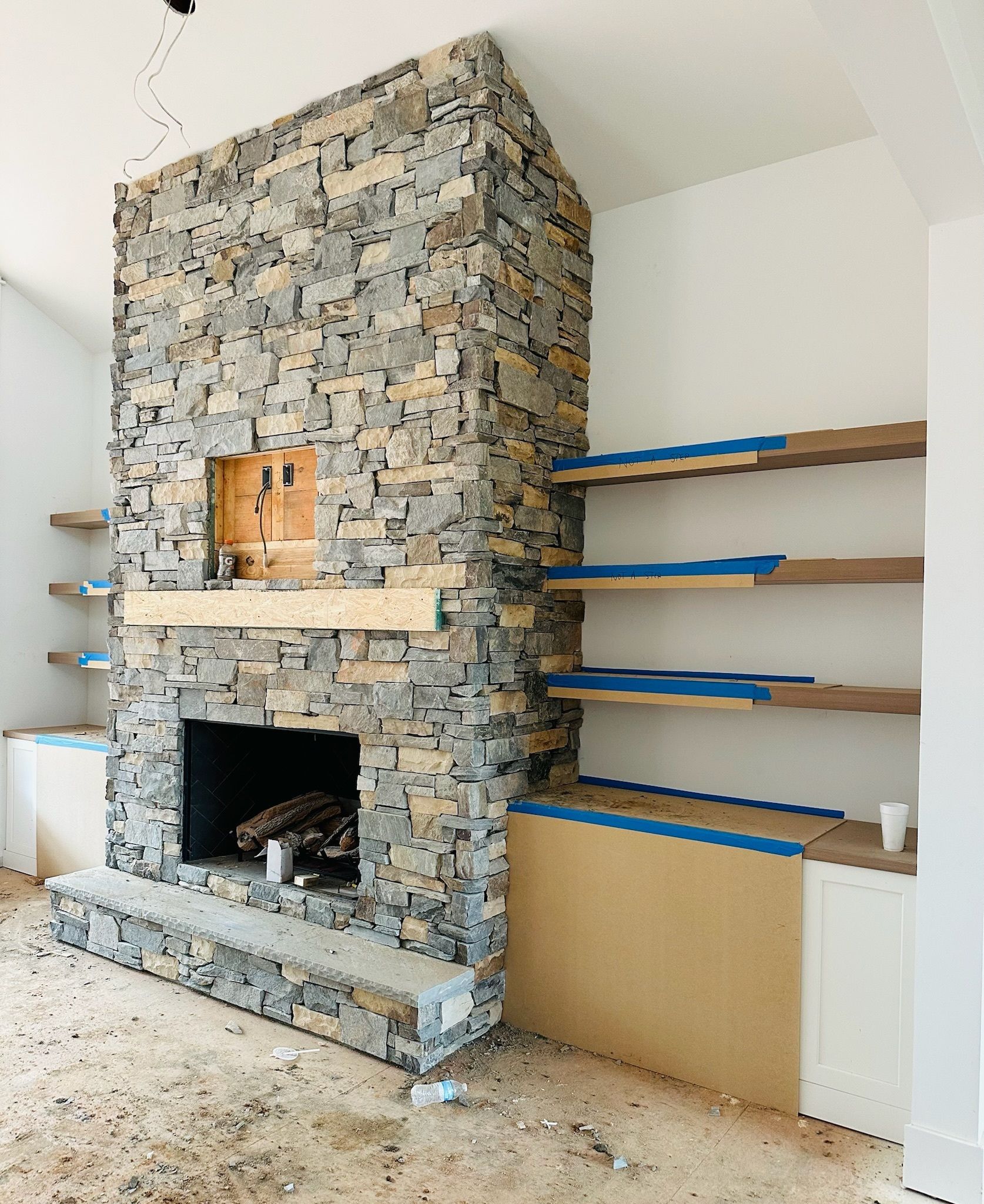 Stone fireplace with wooden mantel and built-in shelves; construction in progress.
