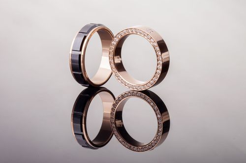 Two gold rings with black accents standing upright on a reflective surface.