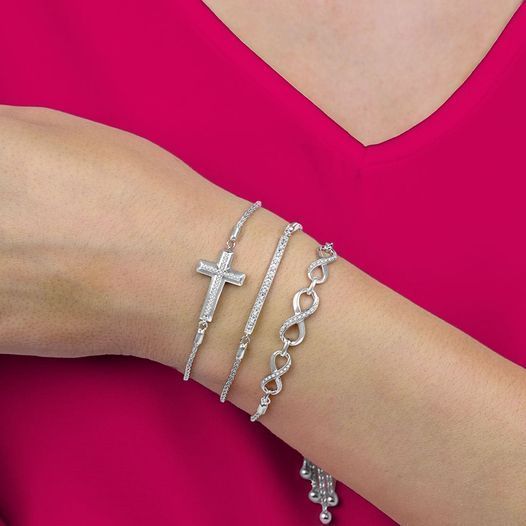 Silver cross and chain bracelets on a wrist against a bright pink top.