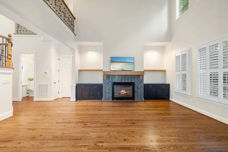 Spacious living room with fireplace, built-in shelves, hardwood floors, and large windows with shutters.