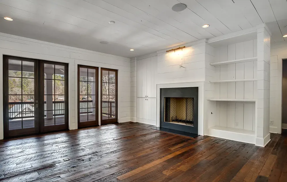 Empty living room with dark hardwood floors, white walls, fireplace, and glass doors.