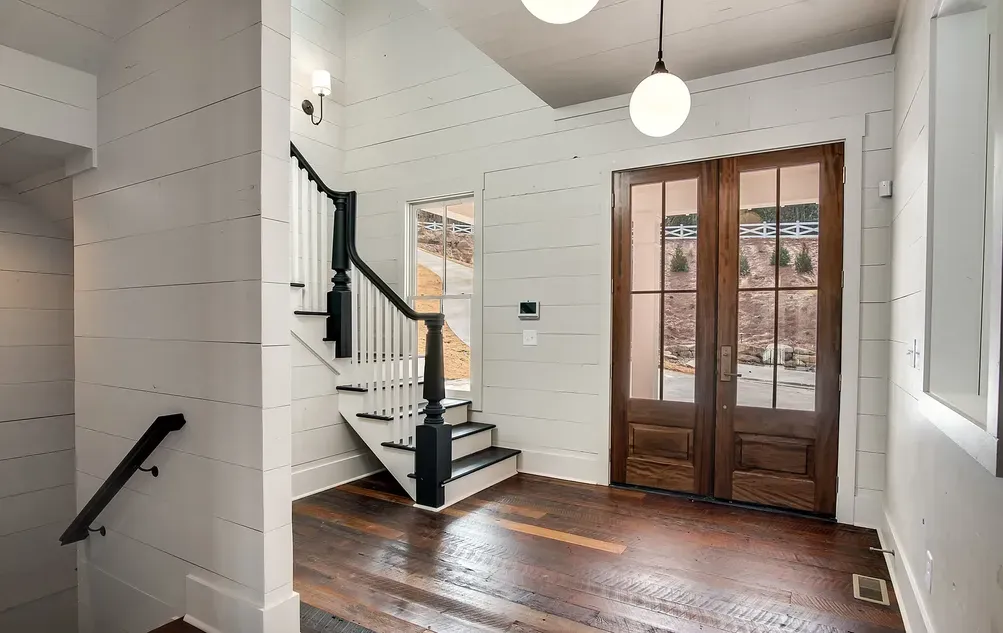Interior of a home entryway with wooden floors, stairs, and glass-paneled doors. White walls and two globe lights.