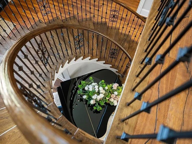 Spiral staircase with wooden steps and black wrought iron balustrade, looking down at a grand piano.