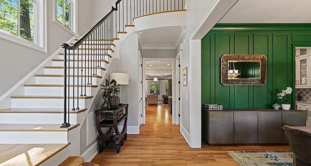 Entryway with staircase, green paneled wall, console table, and hardwood floors.