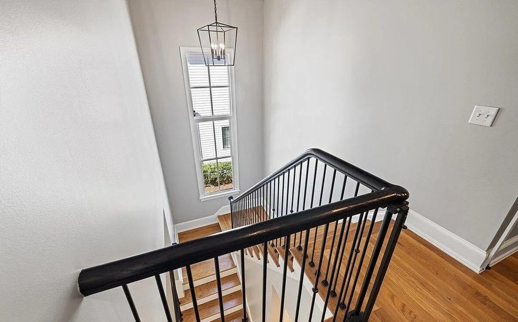 Stairwell with black railing, wooden steps, and a window with natural light. A decorative light fixture hangs above.