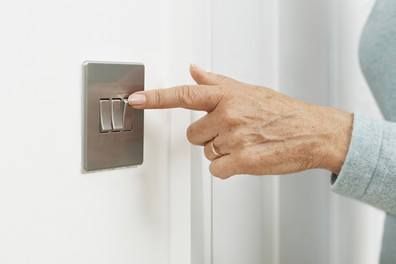 Hand turning on a light switch on a white wall.