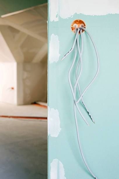 Electrical wires protruding from a wall outlet box in a room under construction.