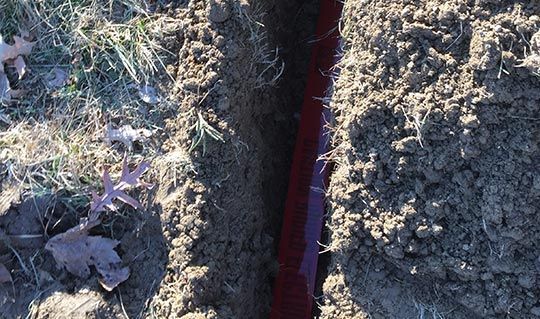 Trench in dirt with a red pipe running through it.