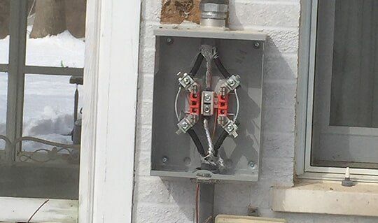 Open electrical meter box on a brick wall with exposed wiring and a silver conduit.