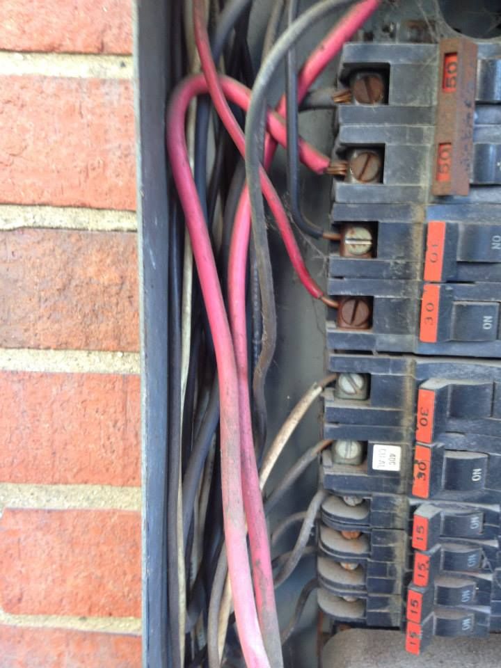 Open electrical panel with red and black wires connected to breakers on a brick wall.