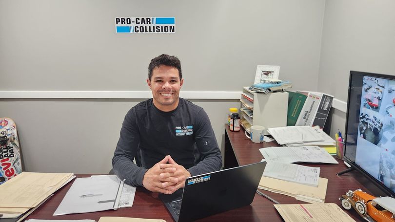 A man is sitting at a desk smiling in front of a laptop computer.