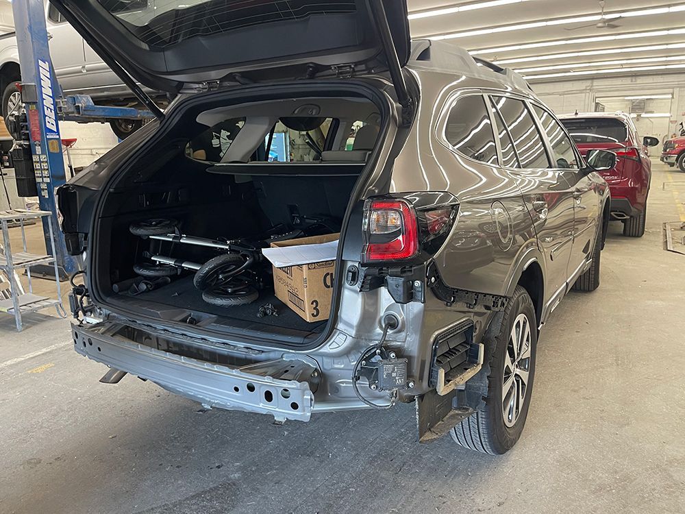 A car is being repaired in a garage with the trunk open.