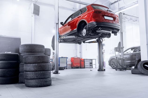Red car lifted on a hoist in an auto repair shop with stacked tires and tools