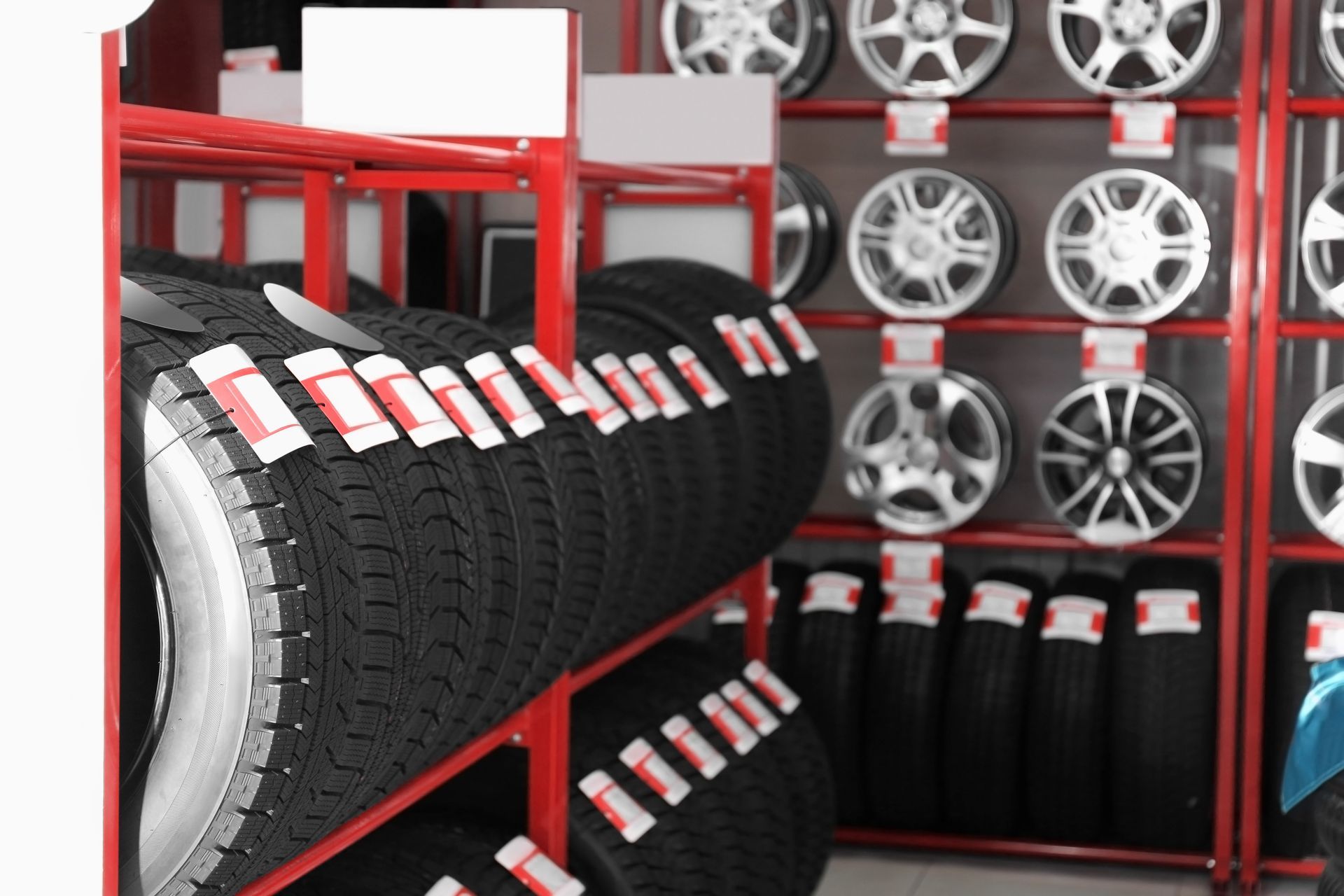 Stacked tires and alloy wheels on red shelving in a tire shop.