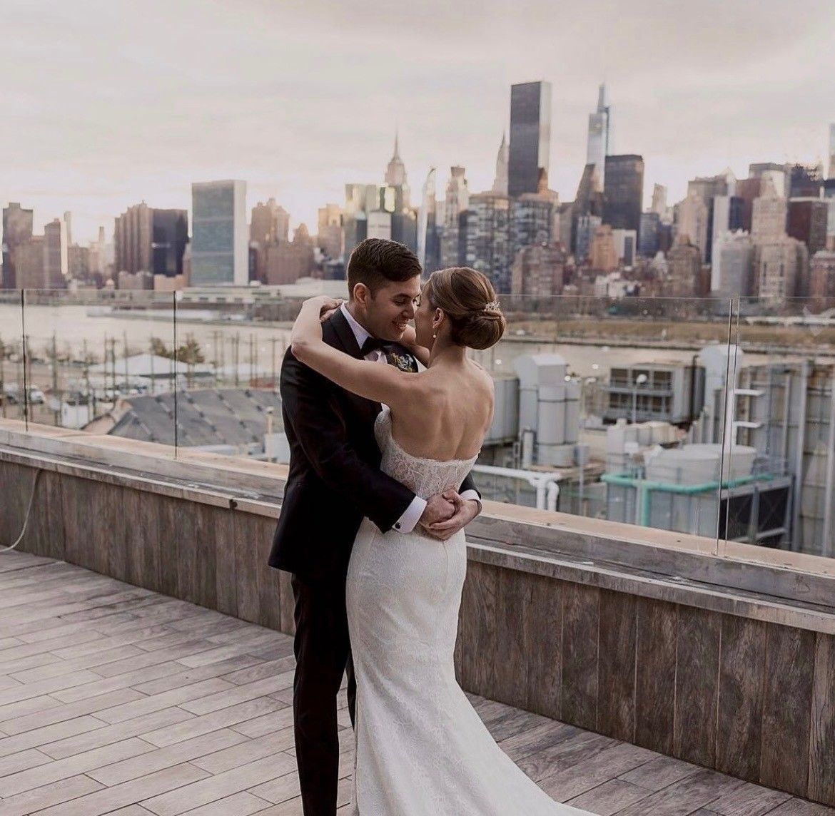 Bride and groom embrace on a rooftop overlooking a city skyline.