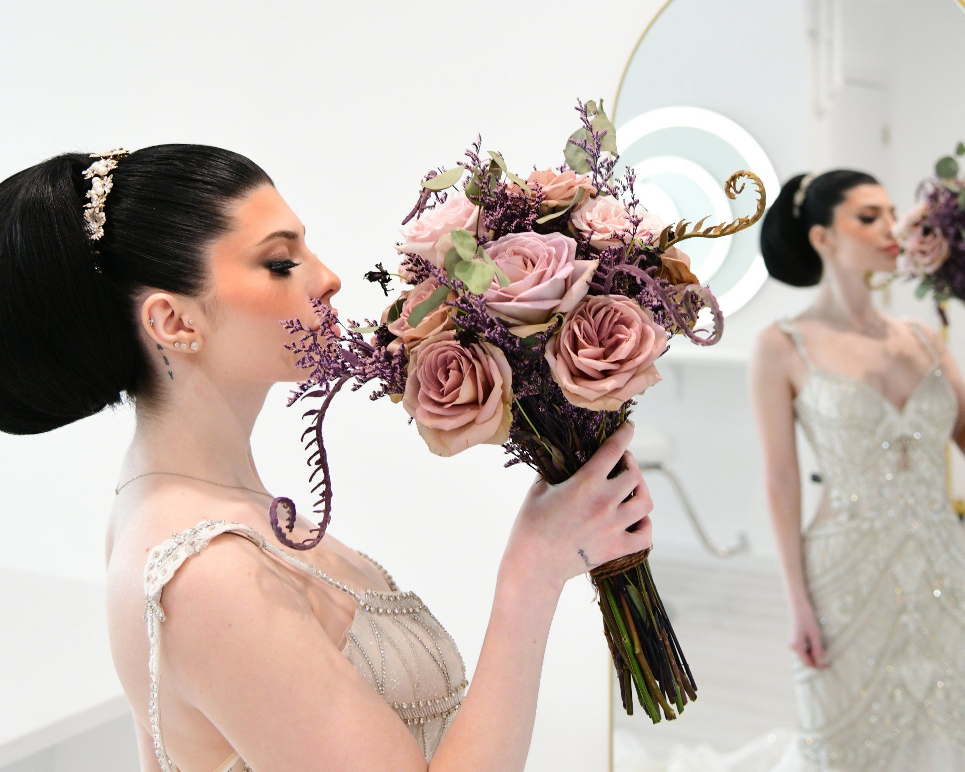 Woman in a beaded gown, holding a bouquet of flowers, looks in a mirror.