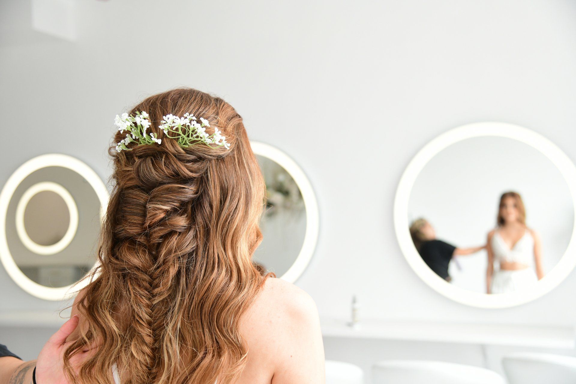 Woman with braided hairstyle, adorned with flowers, looking in a mirror.