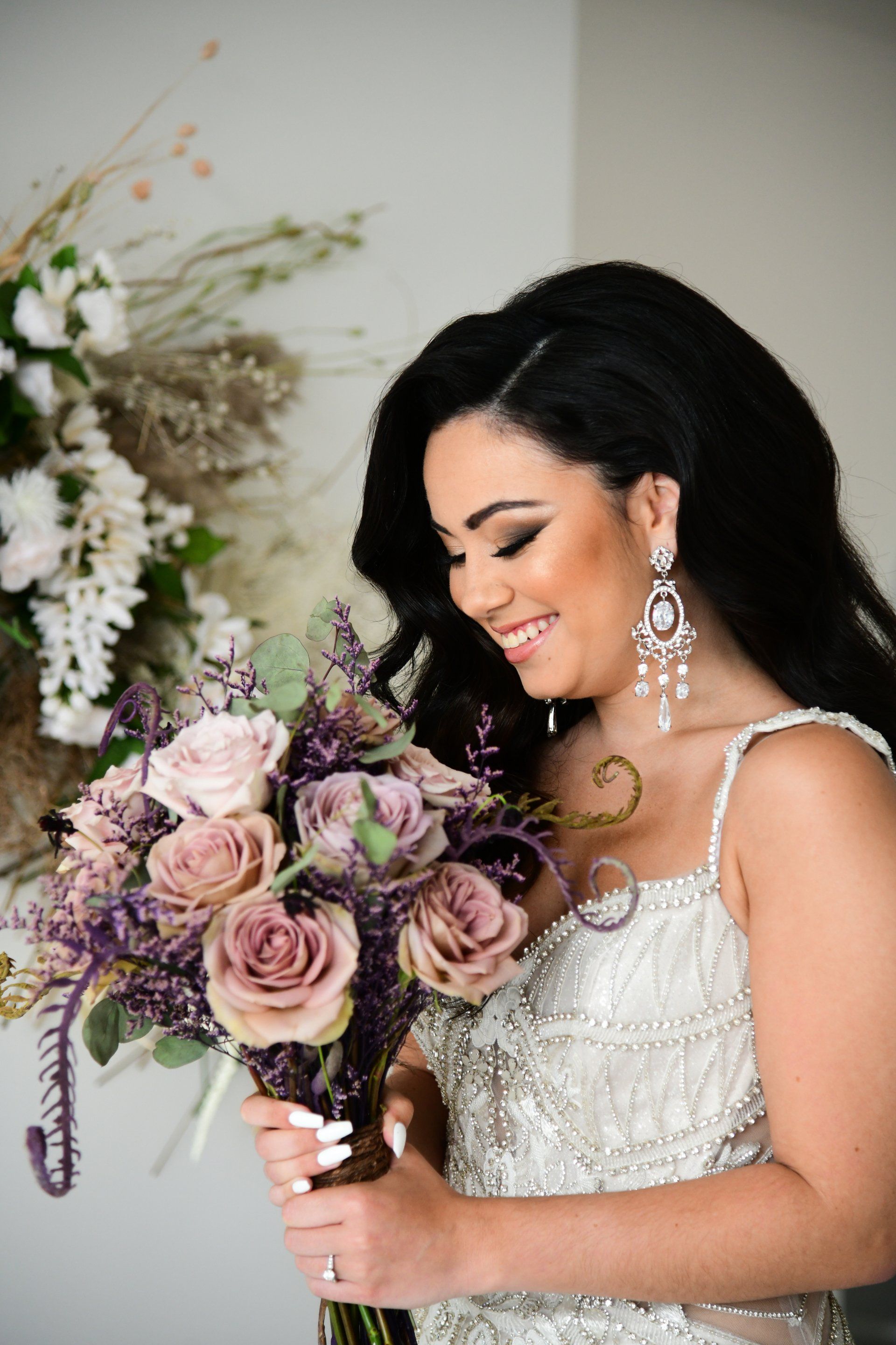 Woman in embellished dress smiles, holding a bouquet of mauve flowers.