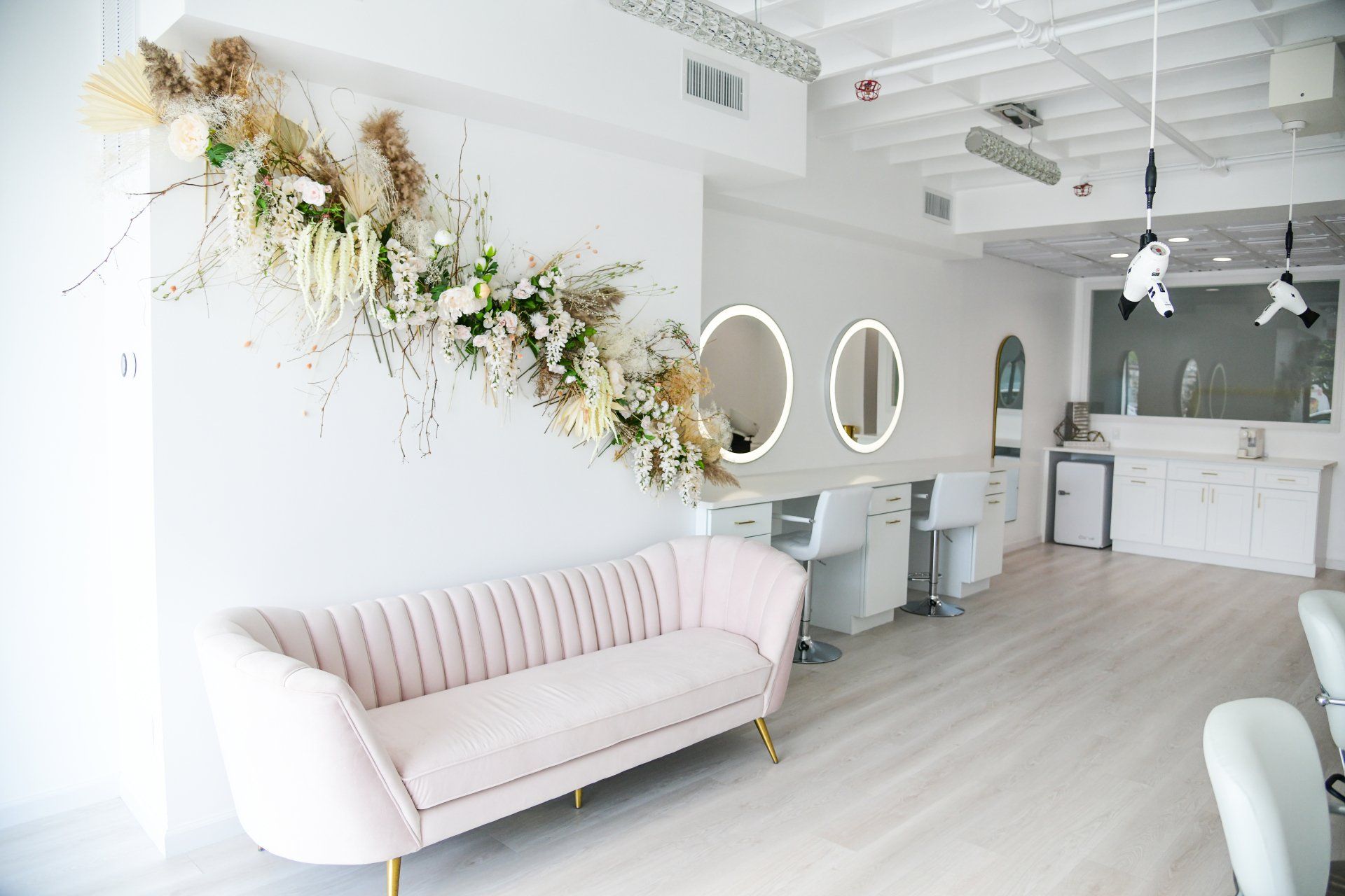 Interior of a hair salon with white walls, pink couch, mirrors, and floral arrangement.