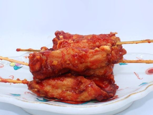 A white plate topped with chicken skewers with sauce on them