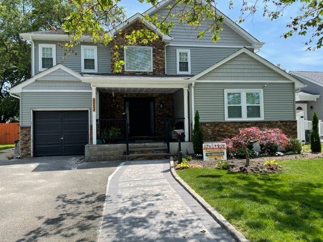 A large gray house with a black garage door is for sale.