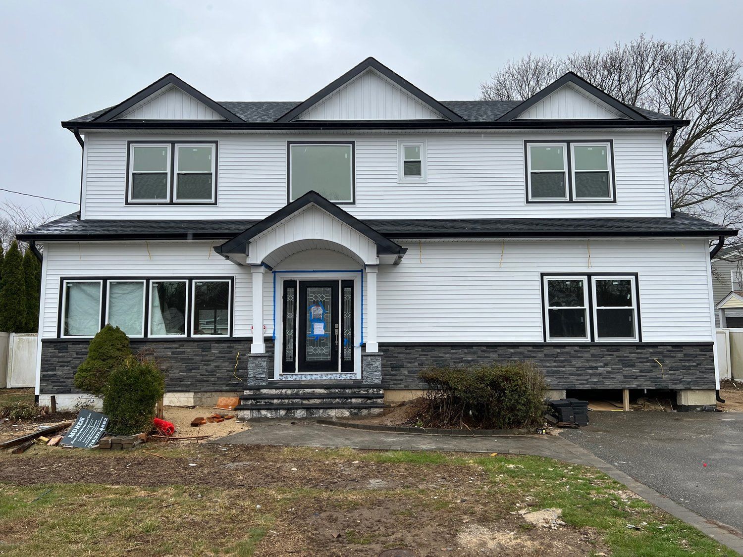 A large white house with a black roof is under construction.