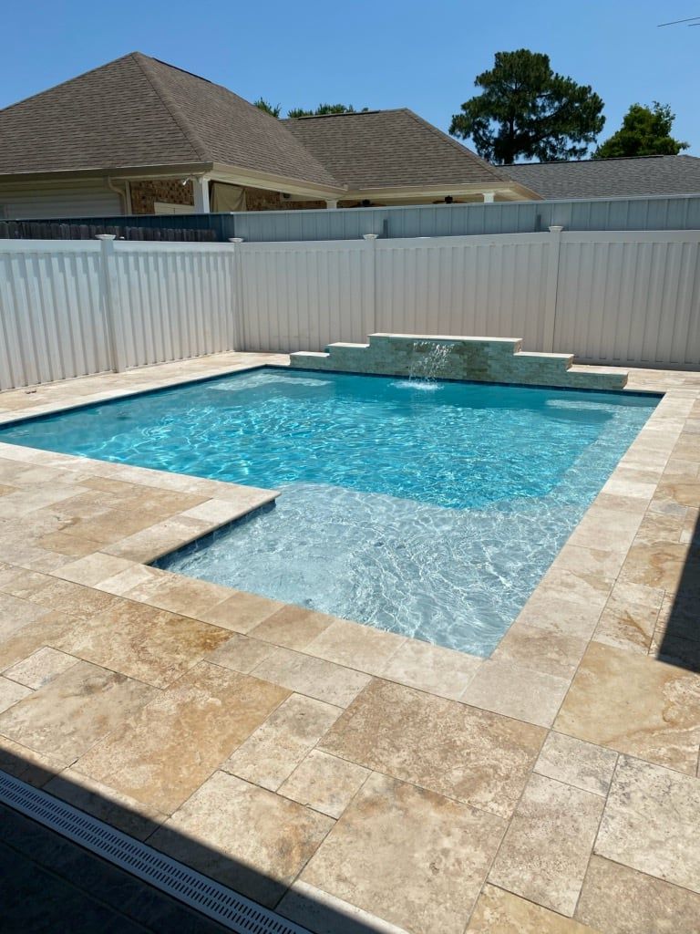 In-ground pool surrounded by travertine tile with raised waterfall wall in Destrehan, LA