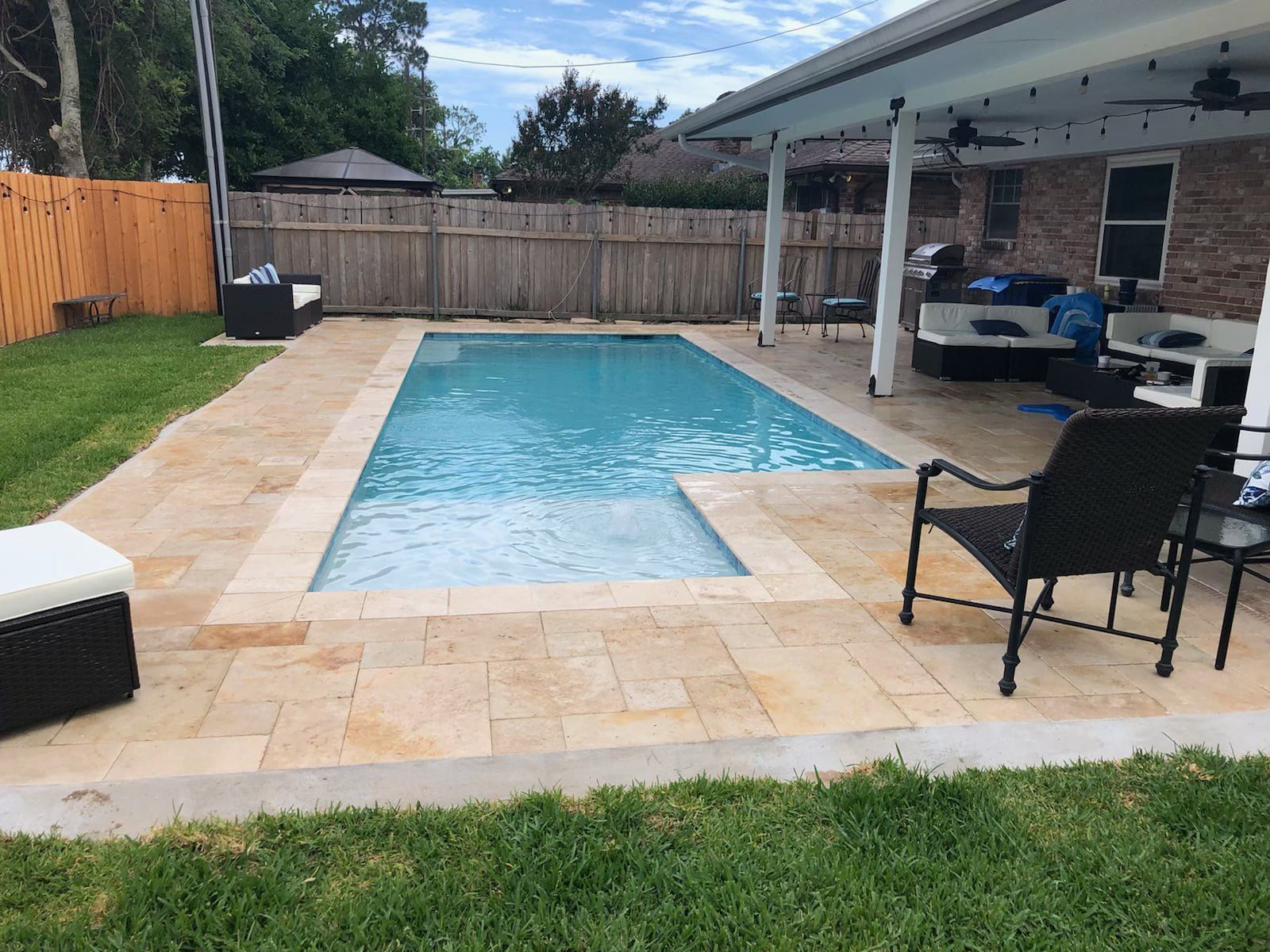 Backyard pool surrounded by travertine patio with lounge chairs in Chalmette, LA
