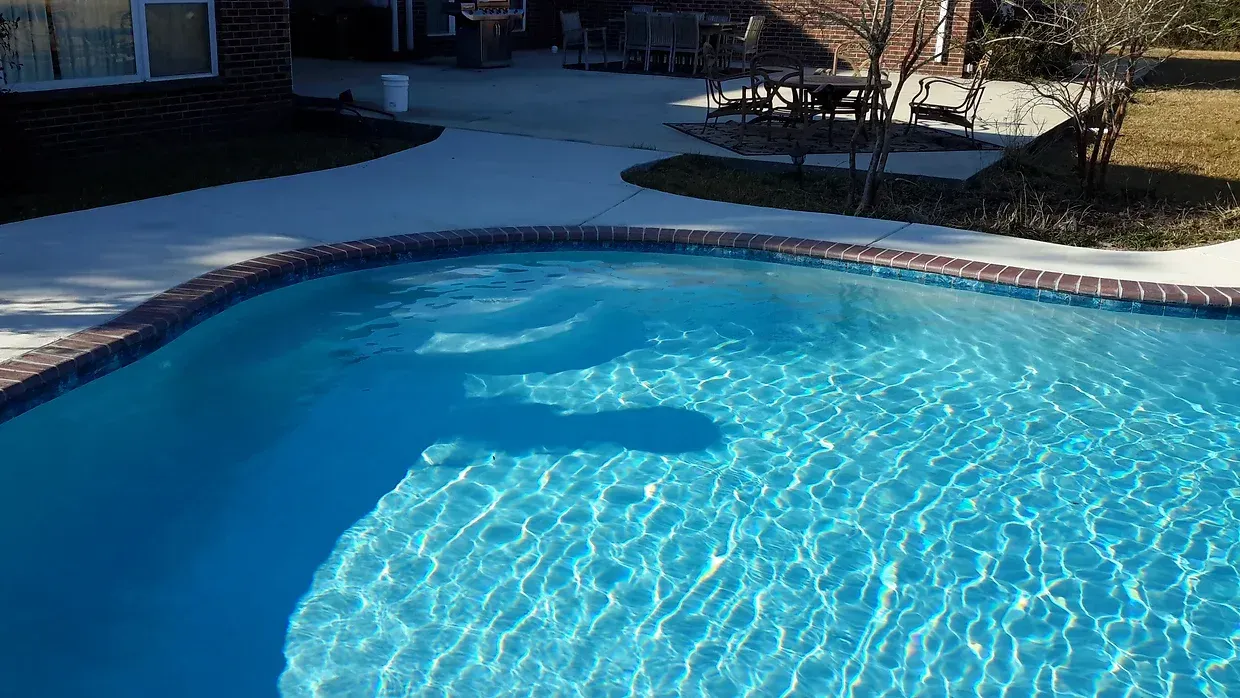 A large, curved swimming pool with brick pavers filled with blue water in a backyard in Covington, LA