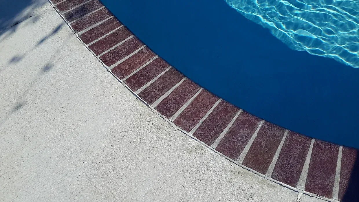 Curved brick border around swimming pool with blue water in Gonzales, LA
