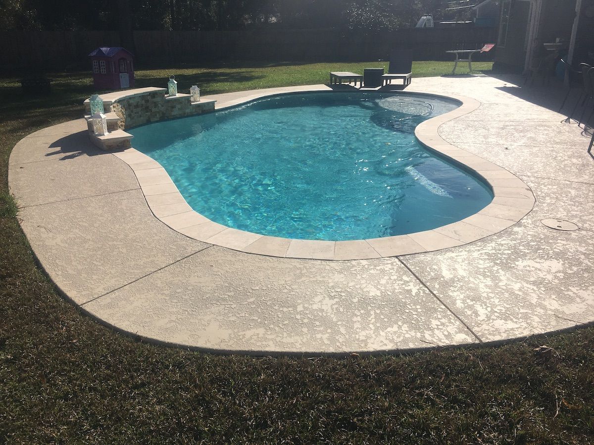 Curved in-ground pool with concrete deck in backyard in Denham Springs, LA