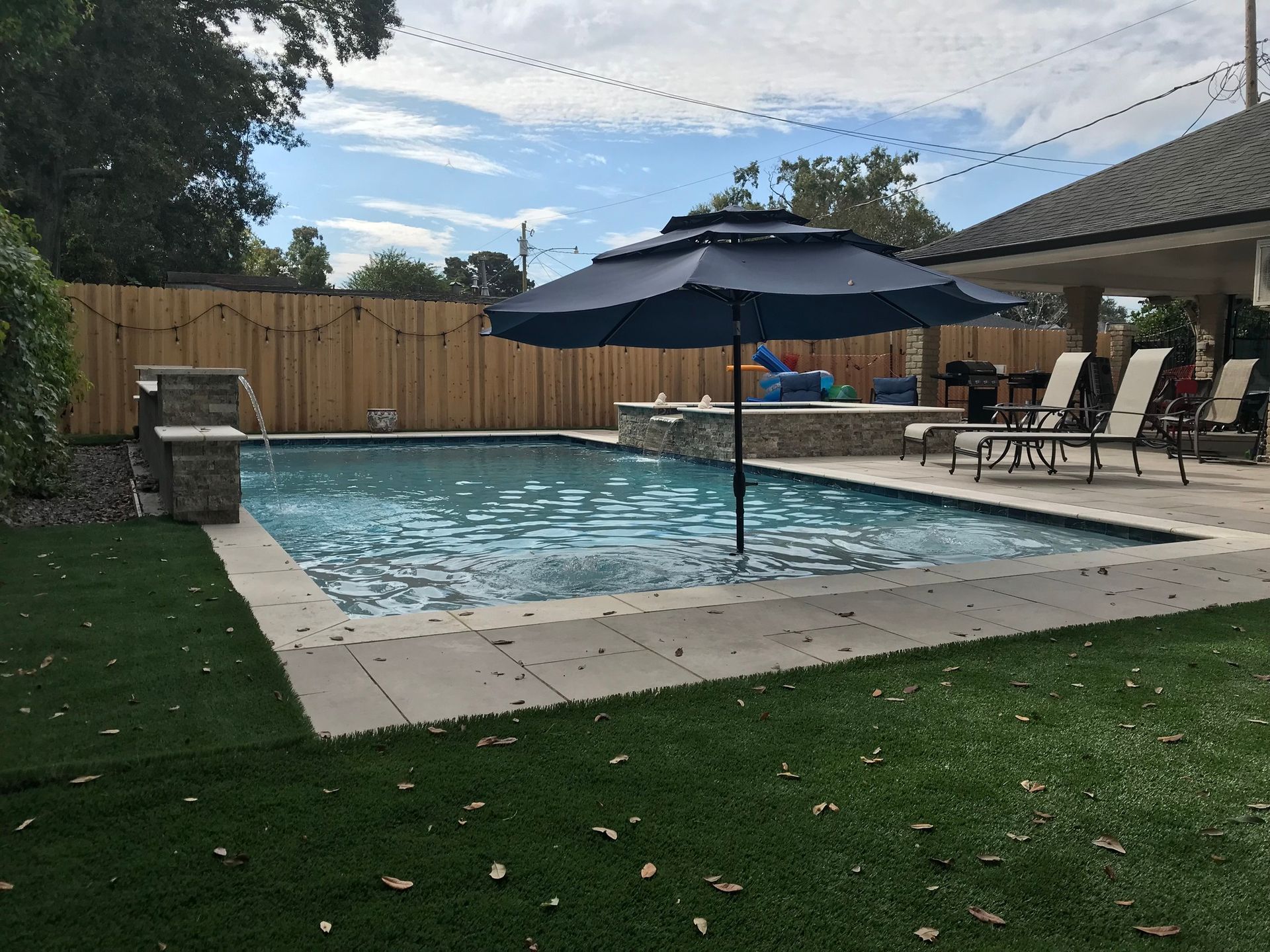 Swimming pool with umbrellas, patio chairs, and nighttime lighting in Covington, LA