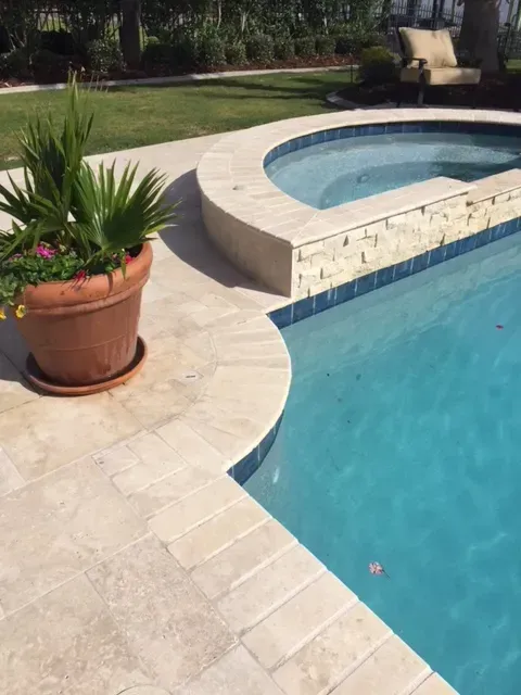 Close-up of curved pool edge with potted plant on travertine patio in Folsom, LA