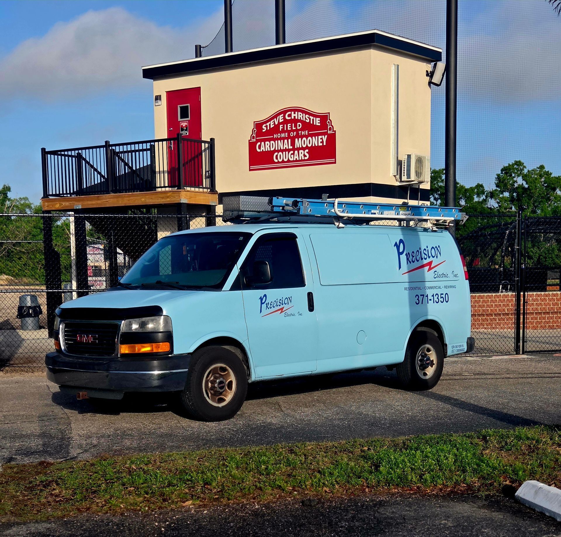 Light blue service van parked outside a cream building with a red sign and black fence.