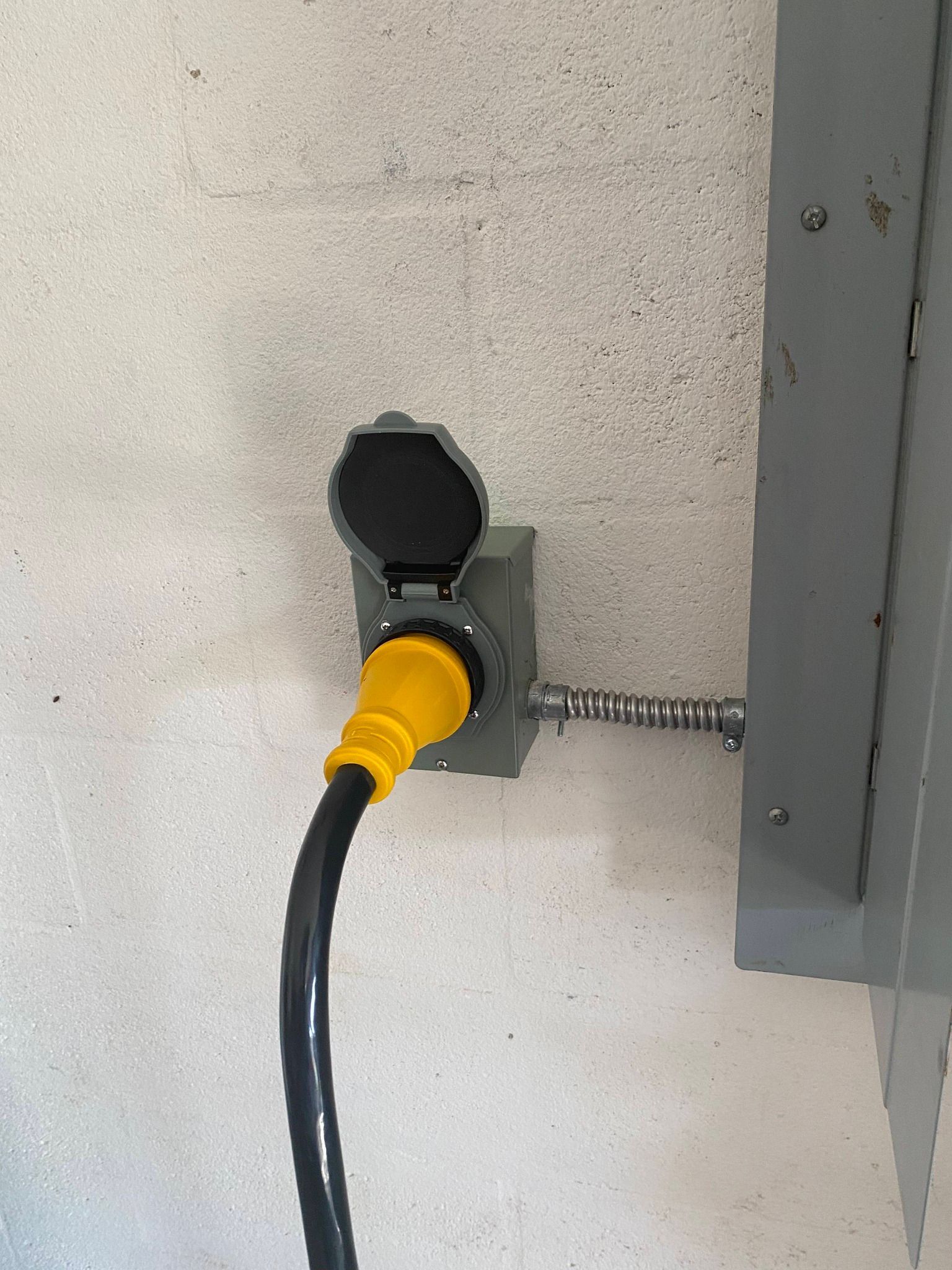 Electrical outlet with yellow plug and black cord mounted on a wall near a metal panel
